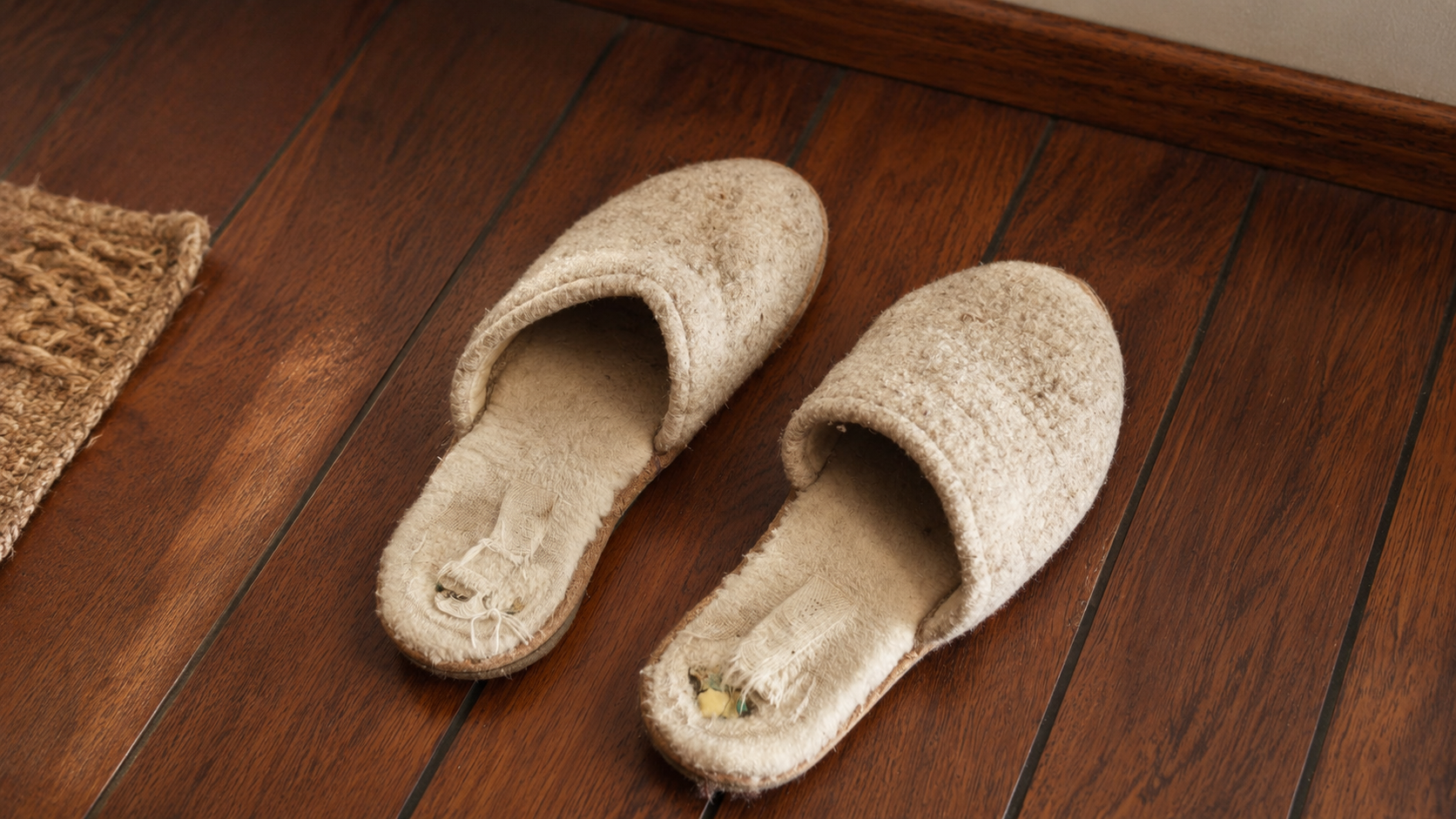 Well-worn natural wool slippers on a wooden floor, showing frayed fabric, soft texture, and years of cozy winter use.