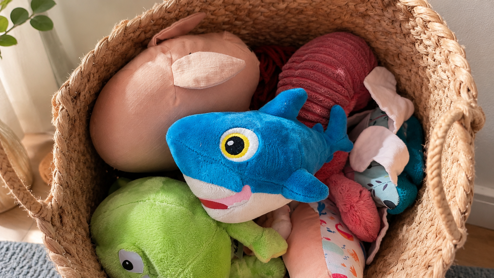 Bright blue DigitalOcean shark plushie nestled in a woven basket full of children’s stuffed toys.